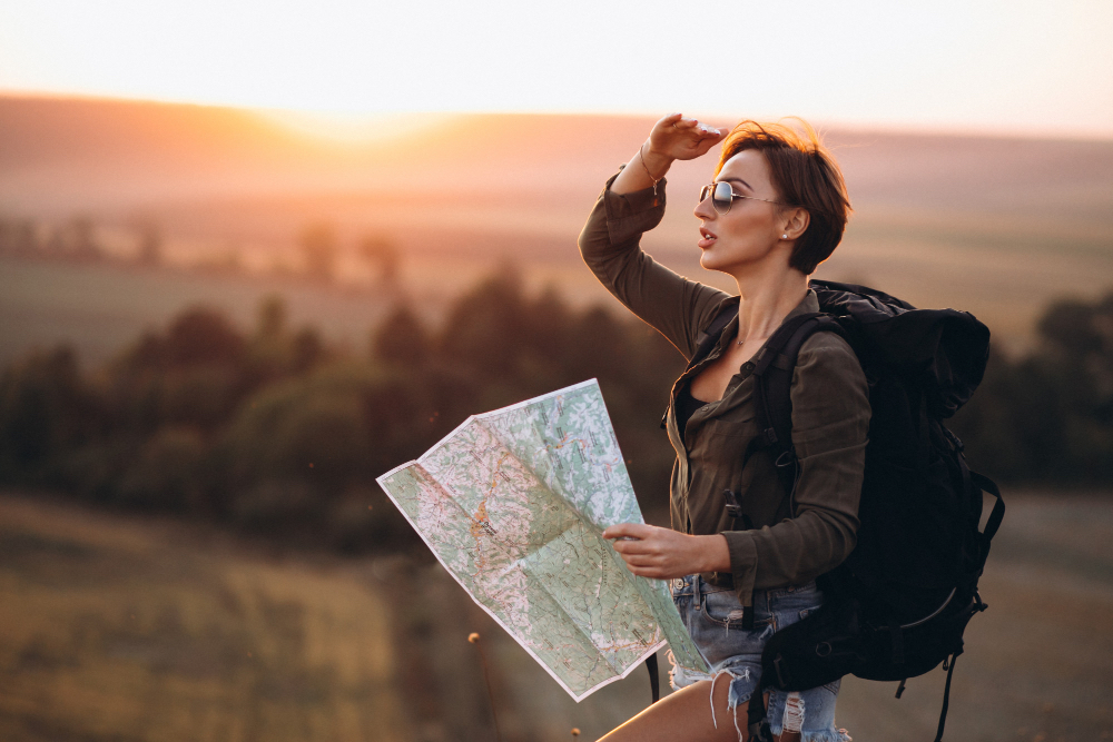 A traveller with a backpack holding a paper map, looking out over hills at sunset