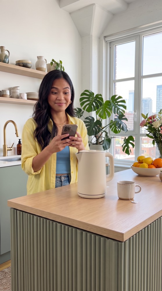 A woman checking her phone while the kettle boils